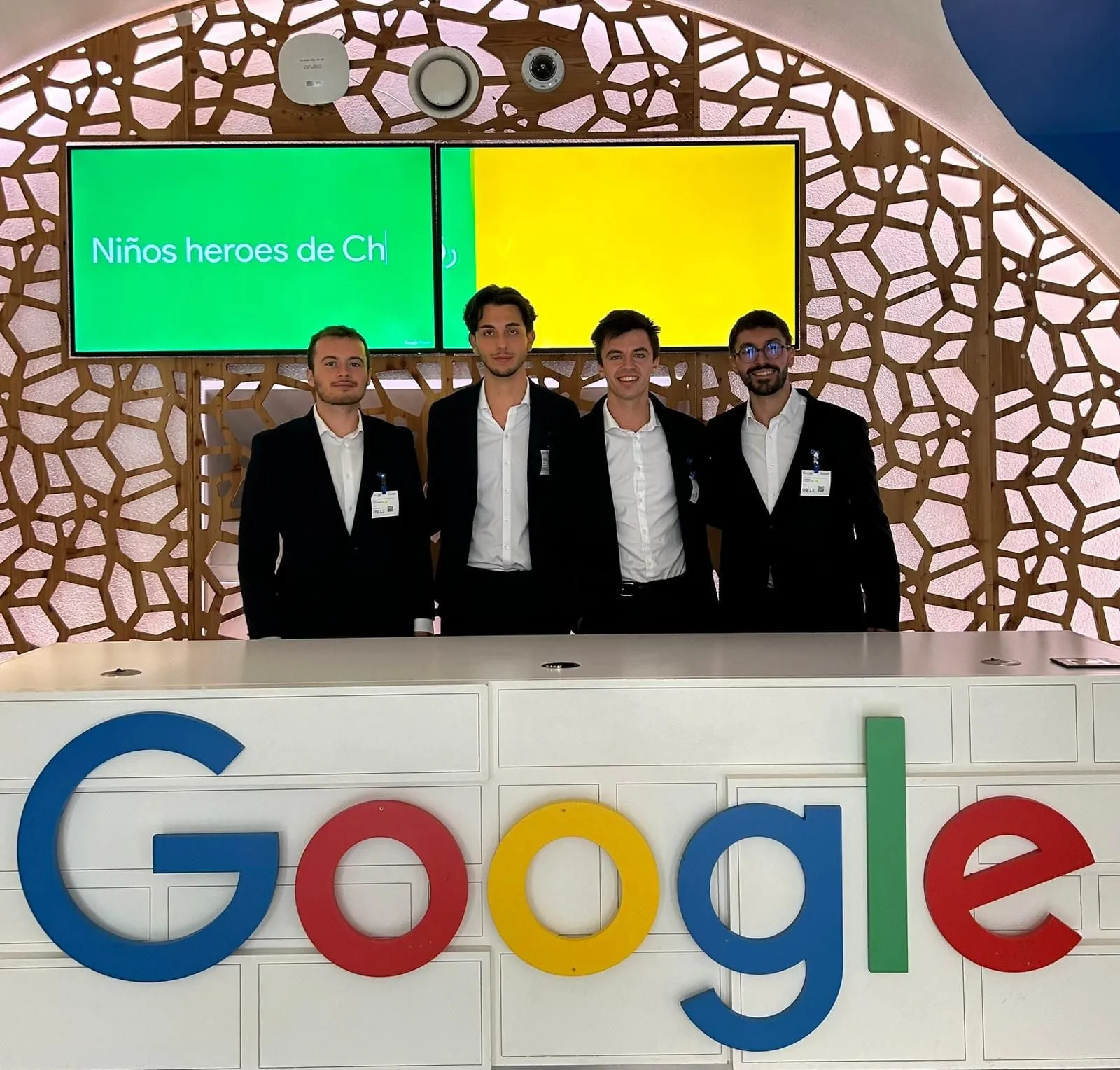 The four team members in suits, standing behind the Google welcome desk at Google’s Paris office